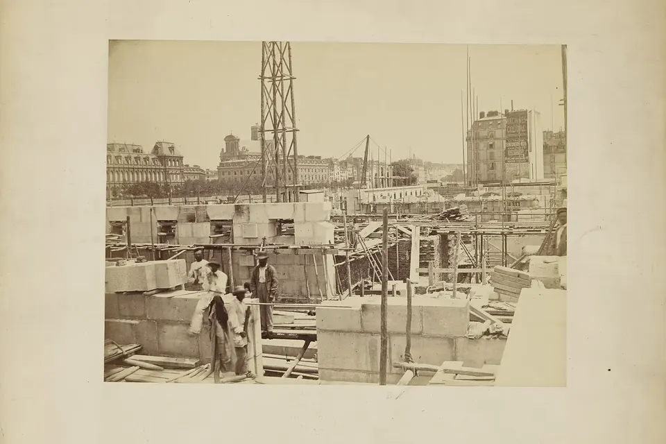 Photographie ancienne d'un chantier parisien avec des blocs de pierre de taille, des ouvriers et des échafaudages en bois