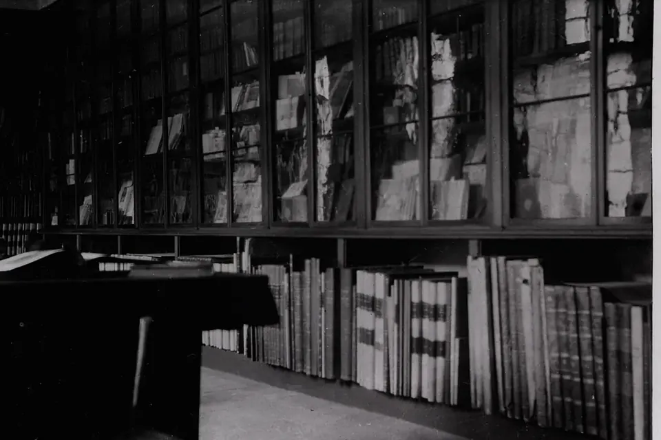 Photographie ancienne en noir et blanc de rayonnages chargés de livres et de vitrines dans une bibliothèque