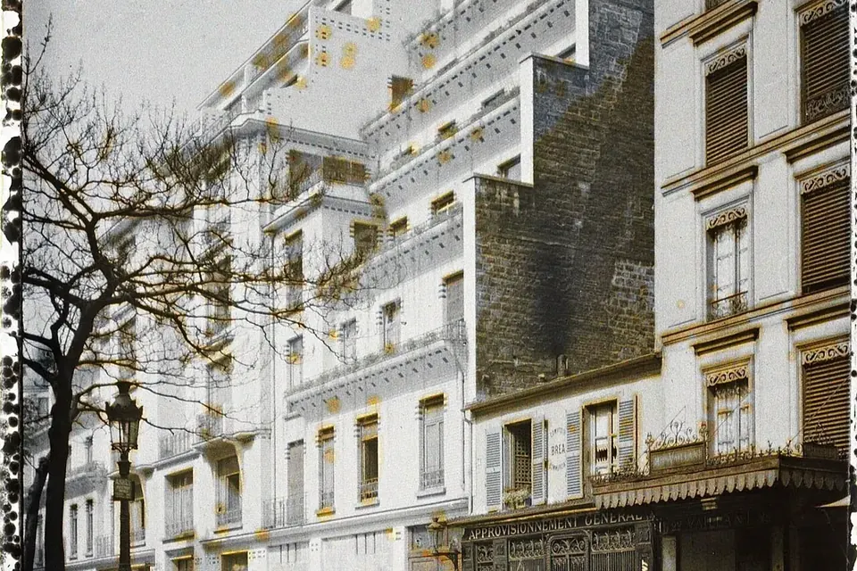 Photographie ancienne en couleurs d'une rue parisienne où un immeuble blanc en gradins, revêtu de carreaux, contraste avec les façades voisines