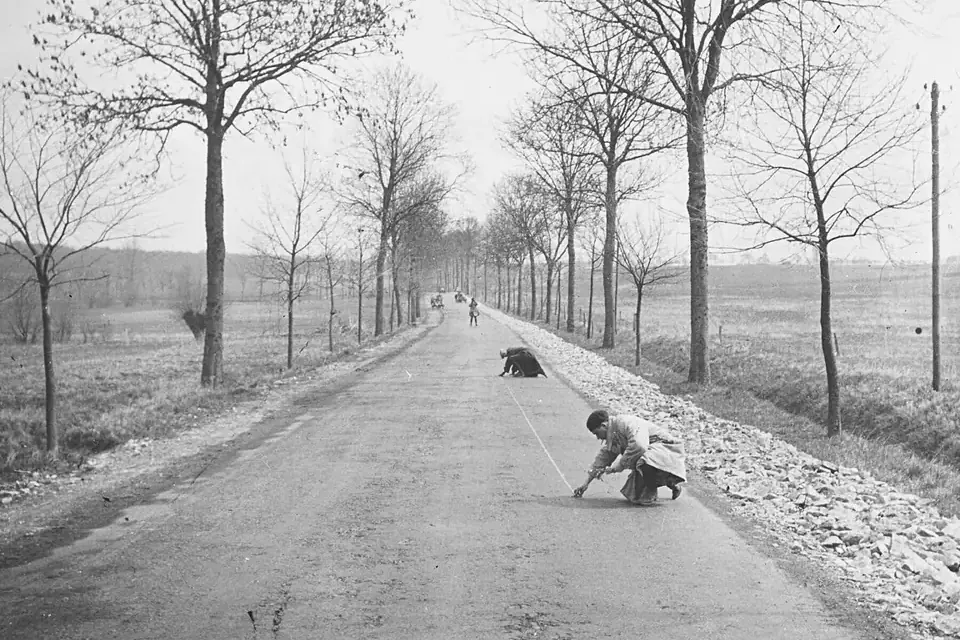 Photographie ancienne de deux hommes tendant un long ruban de mesure sur un terrain en pente, près d'un poteau de repère