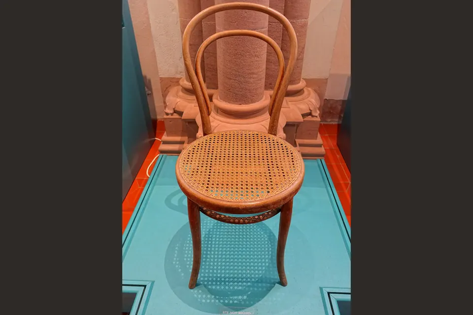 Chaise en bois courbé à dossier arrondi et assise cannée, exposée dans une vitrine de musée